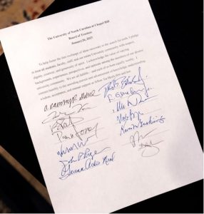 Photo of document with Trustees' signatures on white letter size paper with blue and black ink and black background.