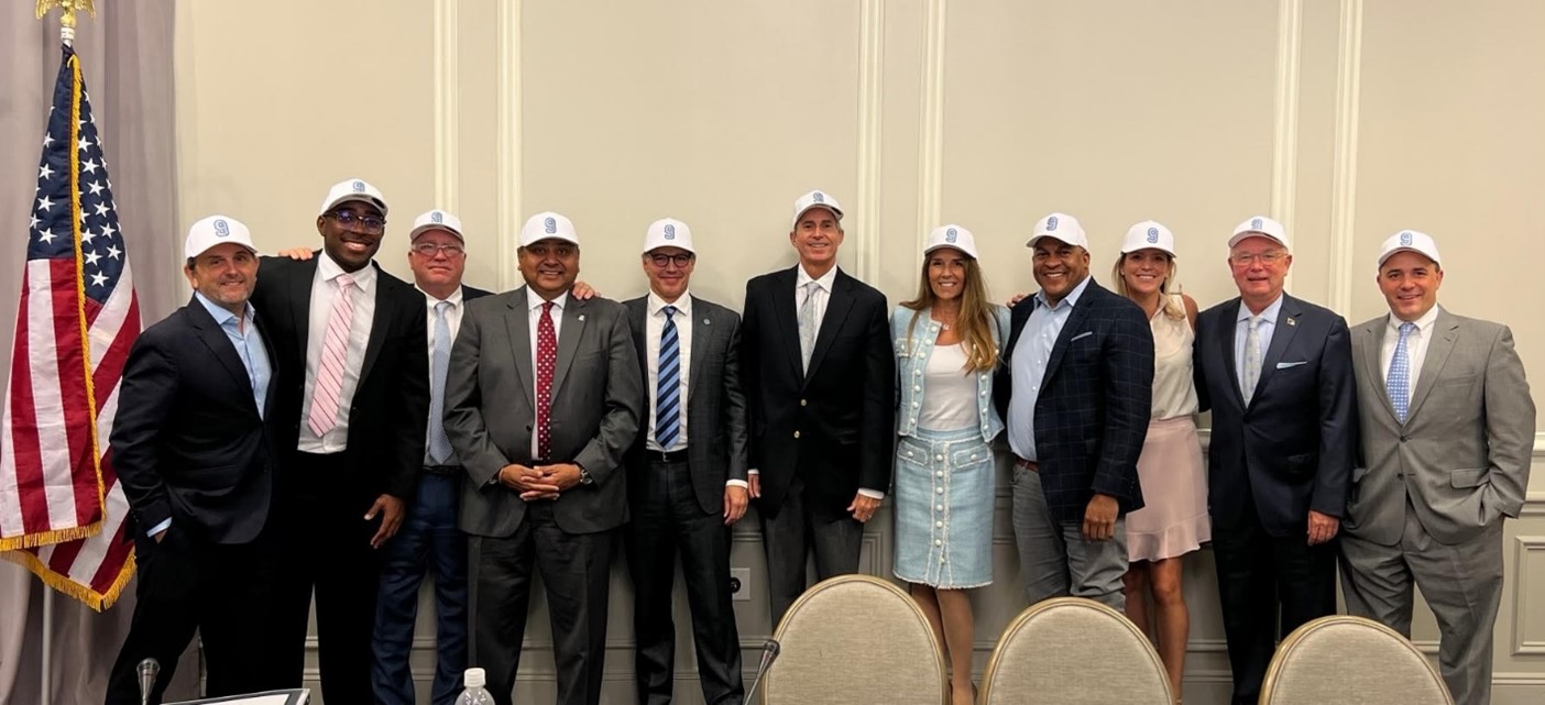 Trustees standing in front of an off-white background wearing white ball caps with the #9 embroidered in Carolina blue in honor of Tez Walker.